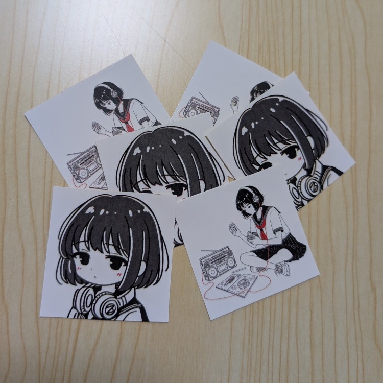 表紙イラストのステッカーとSDモノ子イラストのステッカーを数枚並べた様子
